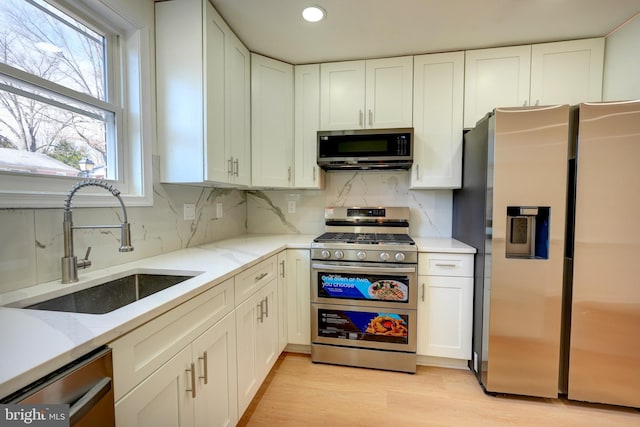 kitchen with light stone counters, appliances with stainless steel finishes, a sink, and white cabinetry