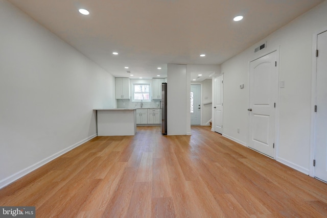 unfurnished living room featuring light wood-type flooring, a sink, baseboards, and recessed lighting