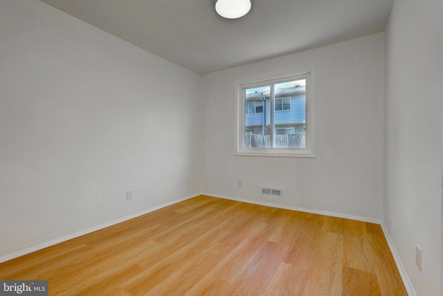 spare room with light wood-type flooring, visible vents, and baseboards