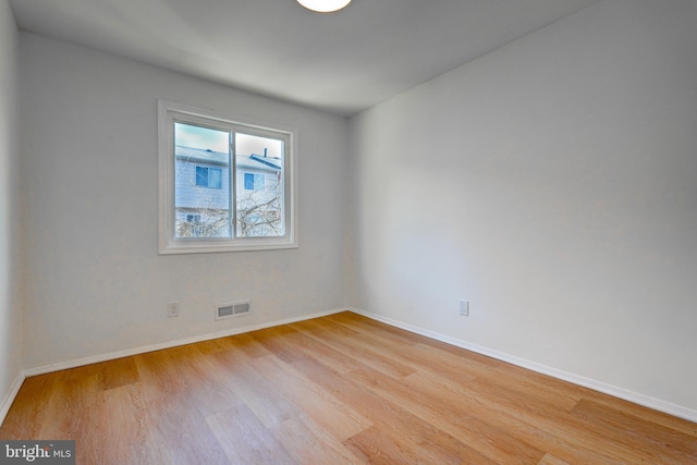 spare room with light wood-type flooring, visible vents, and baseboards