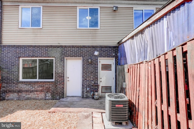 entrance to property with central AC, brick siding, a patio, and fence