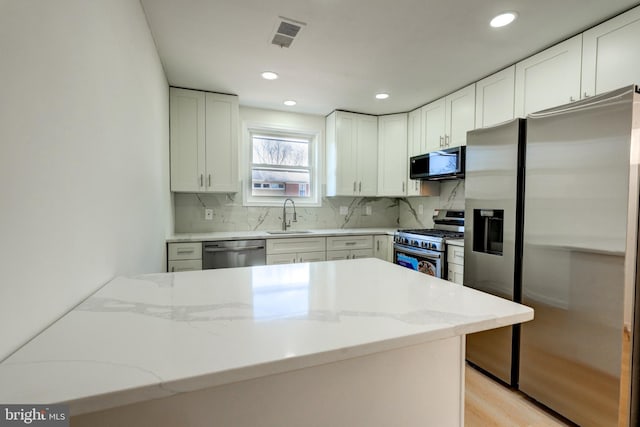 kitchen featuring stainless steel appliances, white cabinetry, a sink, and light stone countertops