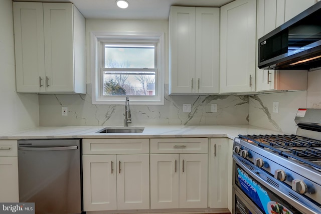 kitchen with white cabinets, appliances with stainless steel finishes, a sink, light stone countertops, and backsplash