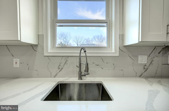 interior details with light stone counters, white cabinetry, a sink, and backsplash