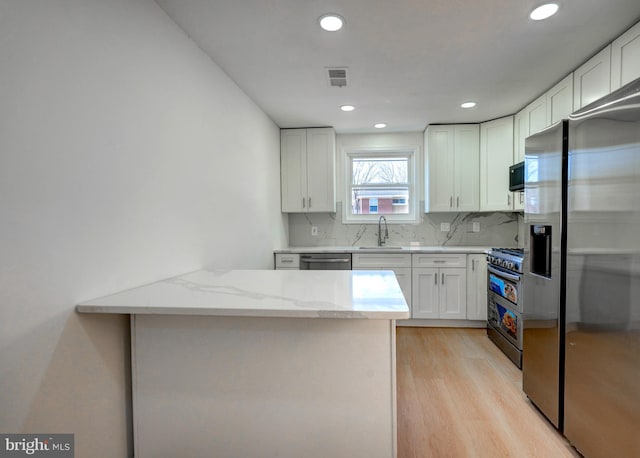 kitchen with a sink, light stone countertops, stainless steel appliances, white cabinetry, and backsplash