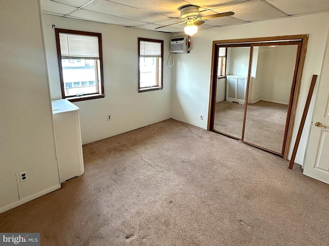 unfurnished bedroom with a paneled ceiling, light colored carpet, a ceiling fan, an AC wall unit, and a closet