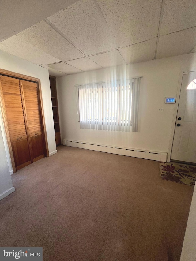 unfurnished bedroom with a baseboard radiator, a closet, carpet flooring, and a paneled ceiling