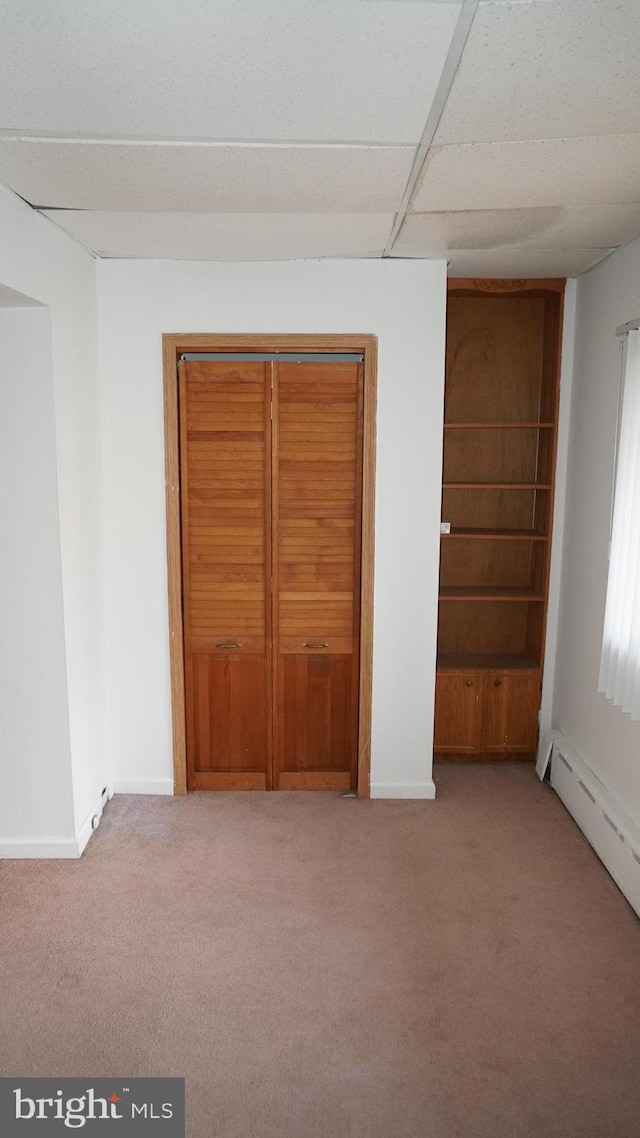 unfurnished bedroom featuring a paneled ceiling, a baseboard radiator, baseboards, and carpet flooring