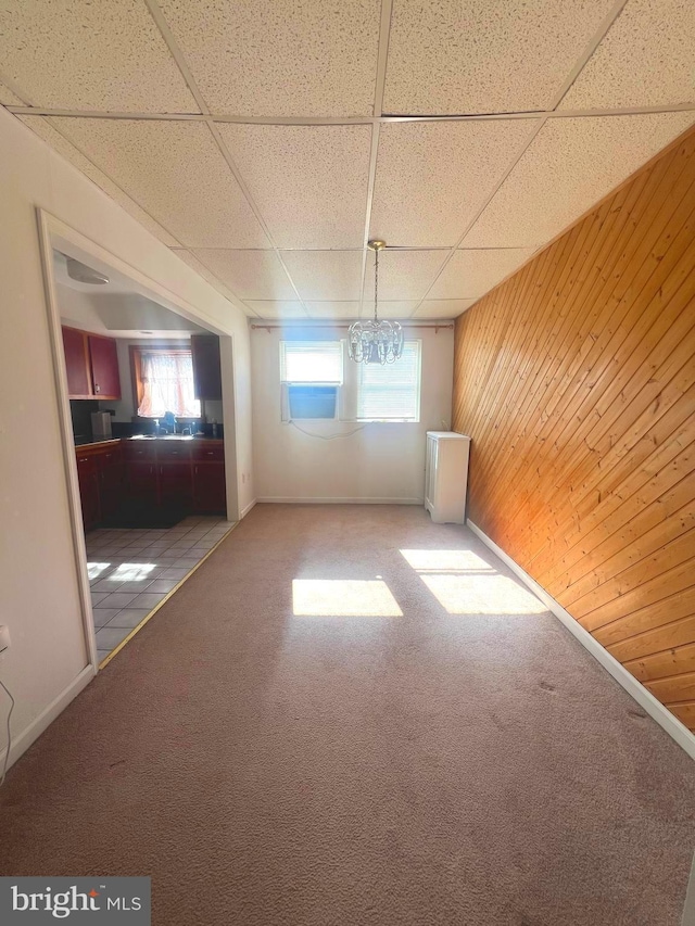 empty room featuring a paneled ceiling, wood walls, and carpet
