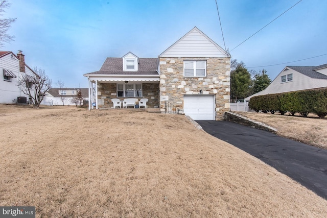 view of front of house featuring aphalt driveway, covered porch, an attached garage, central AC unit, and stone siding