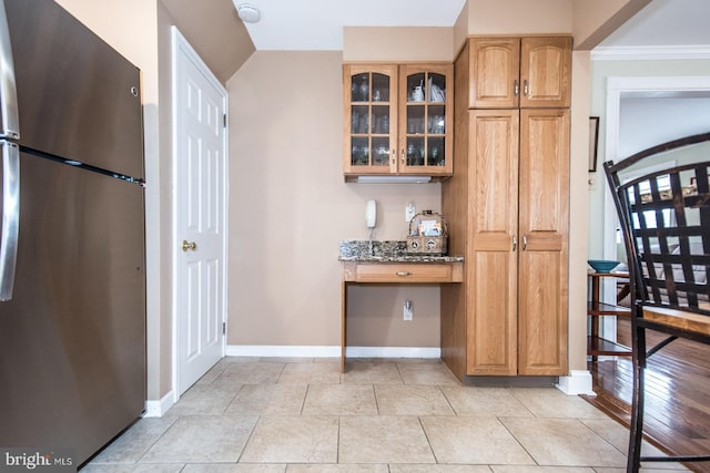 kitchen featuring stone countertops, baseboards, glass insert cabinets, freestanding refrigerator, and vaulted ceiling