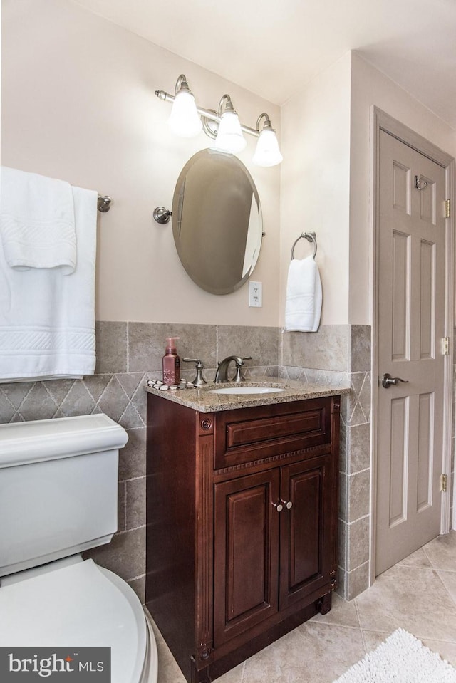 bathroom featuring toilet, vanity, tile patterned flooring, and tile walls