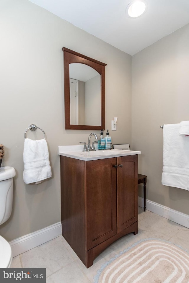 half bath featuring tile patterned flooring, baseboards, vanity, and toilet