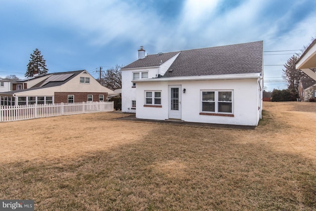 rear view of house with a yard, a chimney, and fence