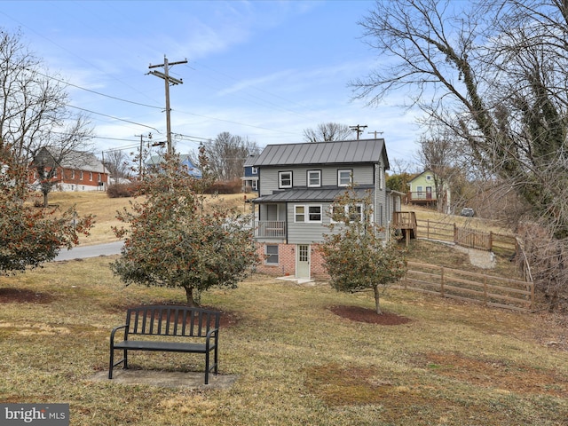 back of property with a yard, fence, metal roof, and brick siding