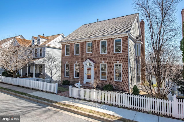 view of front of home with brick siding, a fenced front yard, and a chimney