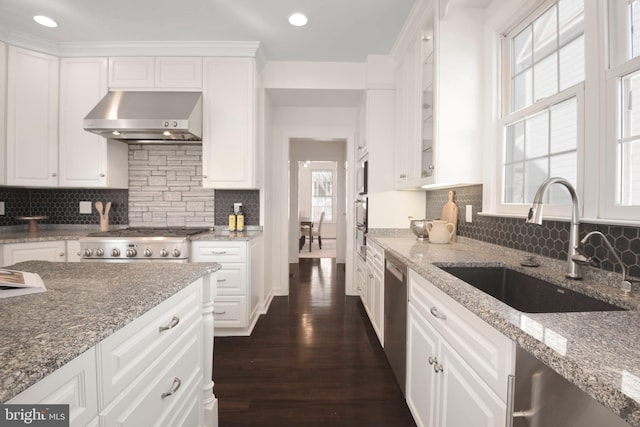 kitchen featuring a sink, stainless steel appliances, white cabinets, wall chimney range hood, and dark wood-style flooring