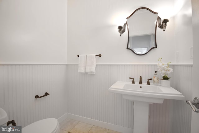 half bathroom featuring toilet, wainscoting, and tile patterned flooring