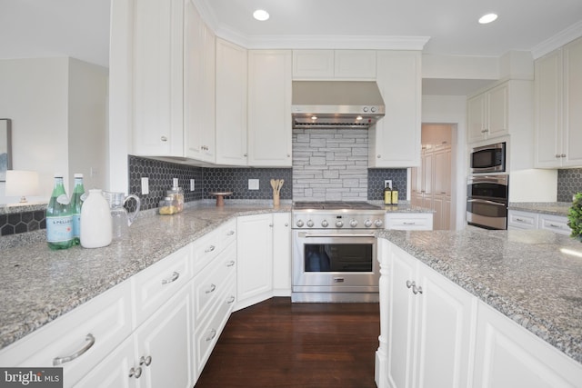 kitchen featuring light stone counters, dark wood-style flooring, appliances with stainless steel finishes, wall chimney range hood, and backsplash