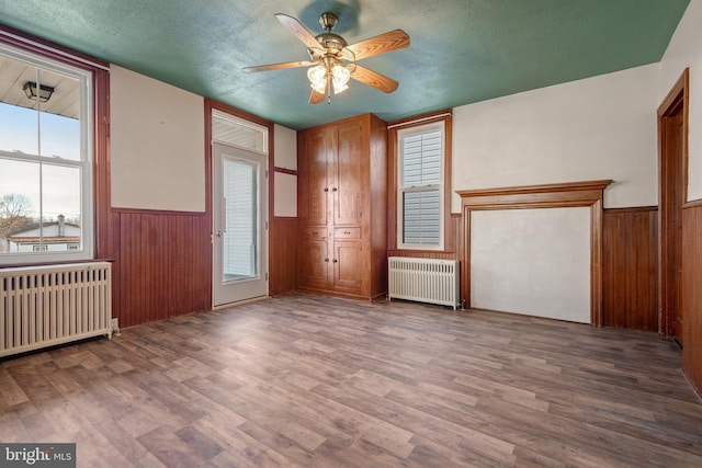 unfurnished room featuring a wainscoted wall, radiator, radiator heating unit, a textured ceiling, and wood finished floors