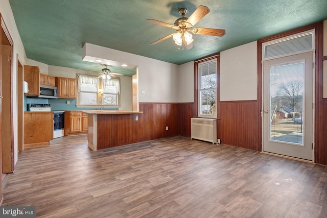 kitchen with a textured ceiling, a wainscoted wall, white electric range, radiator heating unit, and stainless steel microwave