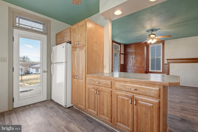 kitchen featuring a ceiling fan, freestanding refrigerator, a peninsula, and wood finished floors