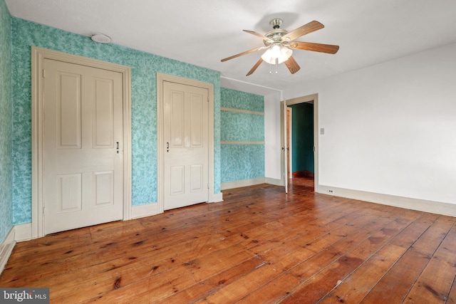 unfurnished bedroom with baseboards, multiple closets, hardwood / wood-style flooring, and wallpapered walls