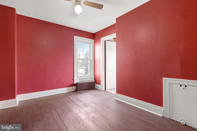 empty room featuring a ceiling fan, baseboards, hardwood / wood-style floors, and radiator heating unit