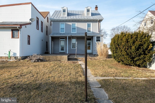 view of front facade with a standing seam roof, a chimney, metal roof, and a front yard