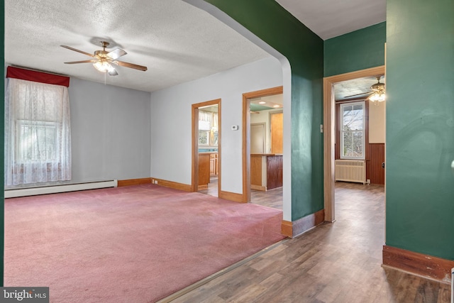 carpeted spare room with radiator, a ceiling fan, baseboard heating, and a textured ceiling