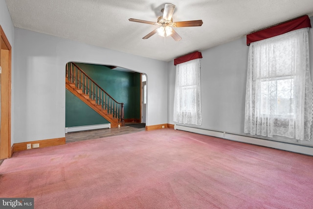 empty room with a textured ceiling, arched walkways, a baseboard heating unit, stairs, and carpet