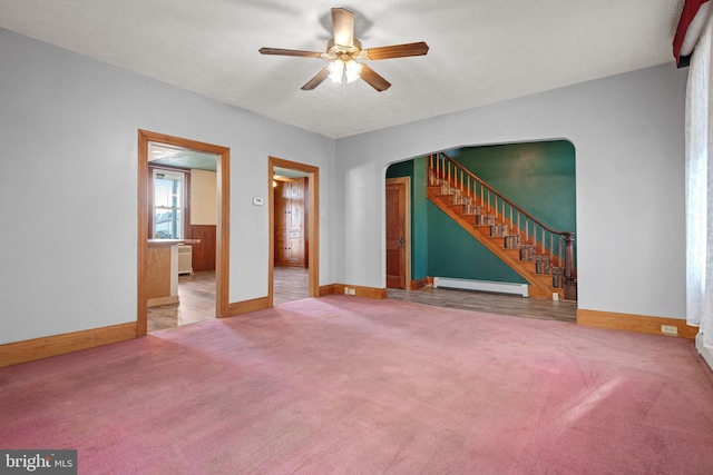 unfurnished room featuring baseboards, arched walkways, stairway, carpet floors, and a baseboard heating unit