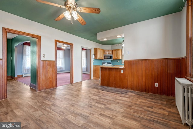 kitchen featuring a wainscoted wall, radiator, stainless steel microwave, wooden walls, and wood finished floors