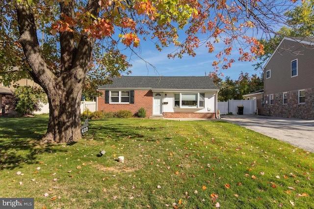 ranch-style house featuring driveway, brick siding, a front lawn, and fence