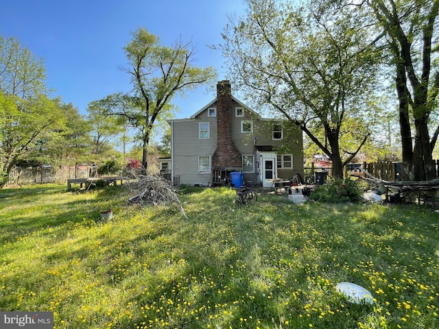 back of property featuring a chimney, fence, and a lawn