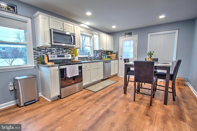 kitchen featuring tasteful backsplash, appliances with stainless steel finishes, light wood-style floors, white cabinets, and a sink