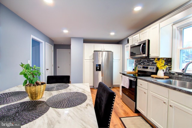 kitchen with stainless steel appliances, tasteful backsplash, light wood-style flooring, white cabinets, and a sink