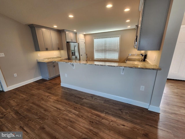 kitchen featuring light stone counters, stainless steel appliances, gray cabinets, dark wood-type flooring, and a peninsula