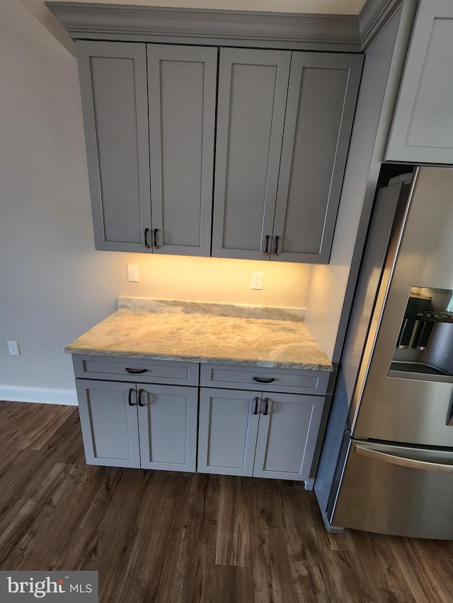 kitchen with light stone counters, gray cabinetry, dark wood-type flooring, stainless steel fridge, and baseboards