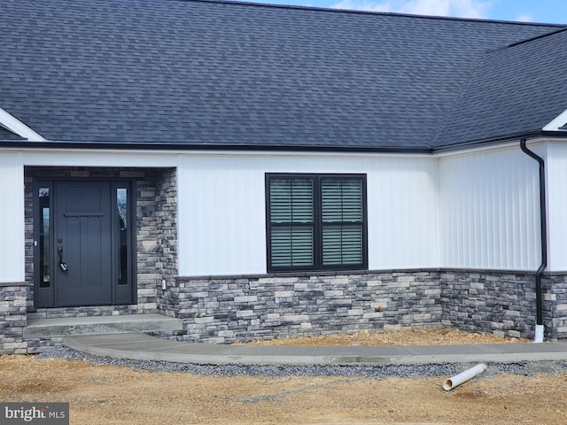 view of exterior entry featuring a shingled roof and stone siding