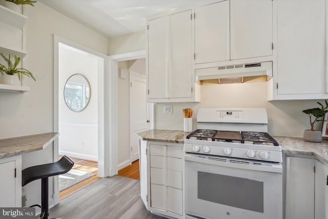 kitchen with white gas range oven, light wood-style floors, under cabinet range hood, white cabinetry, and open shelves