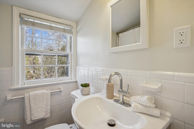 bathroom featuring wainscoting, a sink, tile walls, and toilet