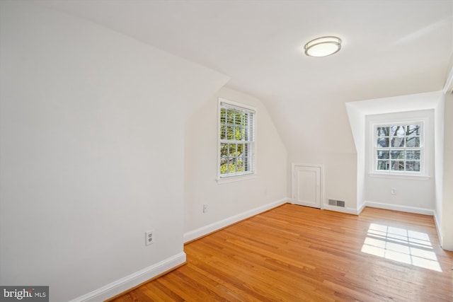 additional living space with light wood-style floors, visible vents, vaulted ceiling, and baseboards