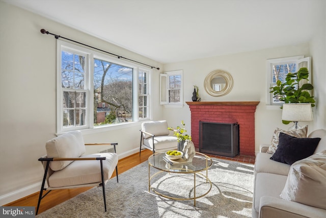 living room featuring a brick fireplace, baseboards, and wood finished floors