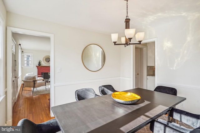 dining room with a brick fireplace, a notable chandelier, and wood finished floors