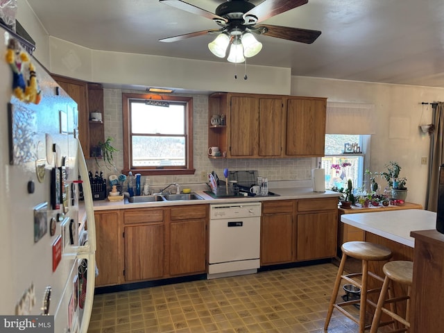 kitchen featuring brown cabinetry, light countertops, white dishwasher, and decorative backsplash