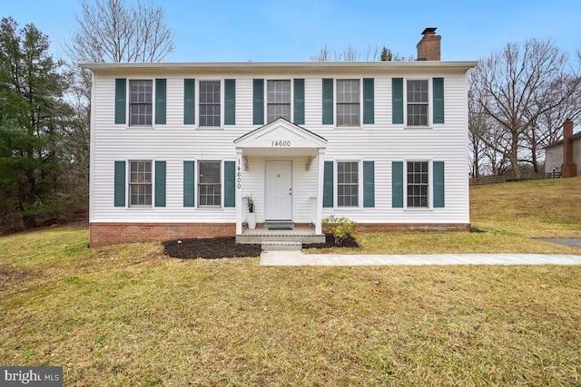 colonial-style house featuring a chimney and a front lawn