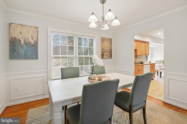 dining room featuring an inviting chandelier, ornamental molding, light wood finished floors, and a decorative wall