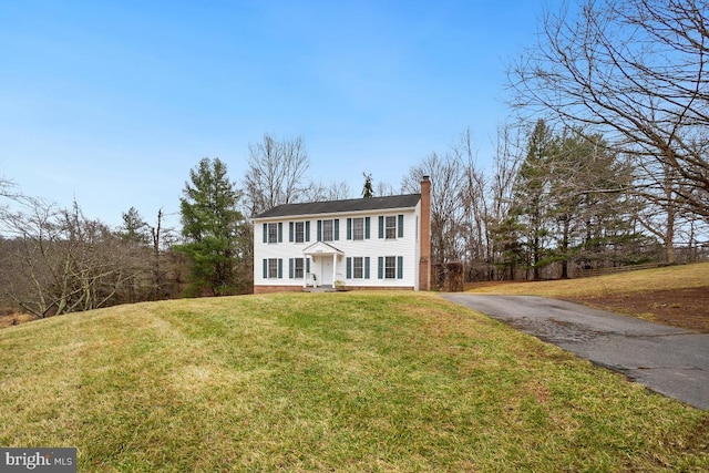 colonial house with driveway, a front lawn, and a chimney