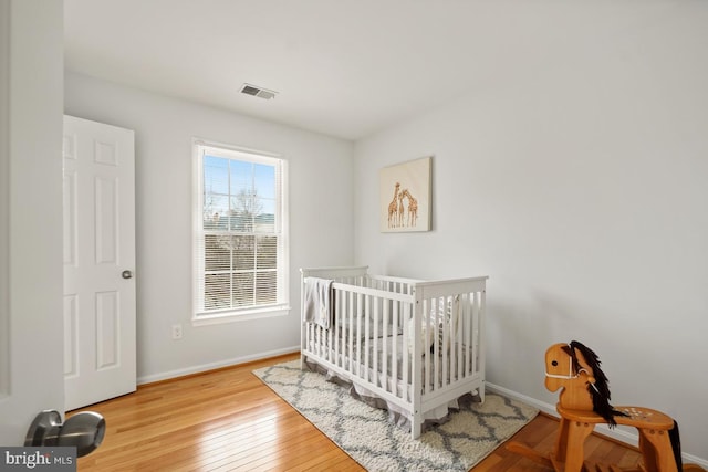 bedroom with hardwood / wood-style flooring, baseboards, visible vents, and a nursery area